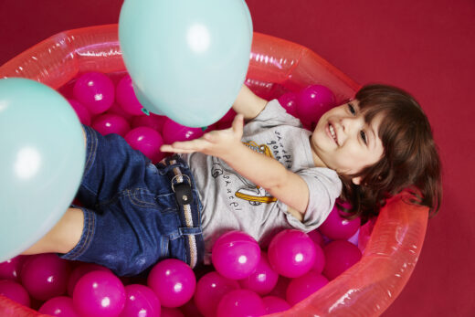 Criança menina com franja em look jeans brincando com boia bolinhas e balão